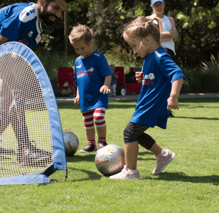 View of children kicking soccer ball into a goal in tennis shoes, practicing soccer outdoors.