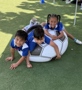 three kids laughing and laying on a blow up soccer ball