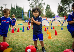 toddlers playing soccer outside between colored cones