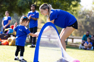 occer Stars coach helping a young child practice soccer by a small goal during an outdoor class.