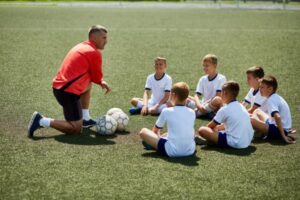 coach kneeling down talking to kids in a soccer class